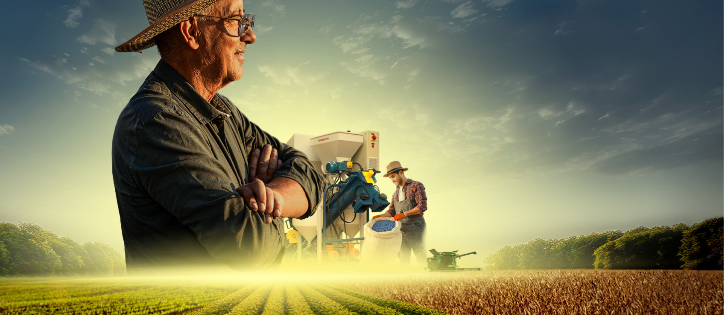 Fazendeiro de braços cruzados olhando para o horizonte em uma plantação ao entardecer.